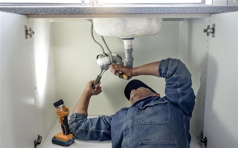 Plumber repairing pipes beneath a bathroom sink in Burbank
